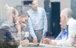 Eine Frau im Businessoutflit erklärt vier Kollegen freundlich einen Sachverhalt.