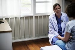 Eine Ärztin im Gespräch mit einer jungen Patienten, die auf einem Bett sitzt