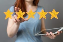Symbolfoto Ranking: Junge Frau hält Tablet in den Händen und gibt eine 5-Sterne-Bewertung ab
